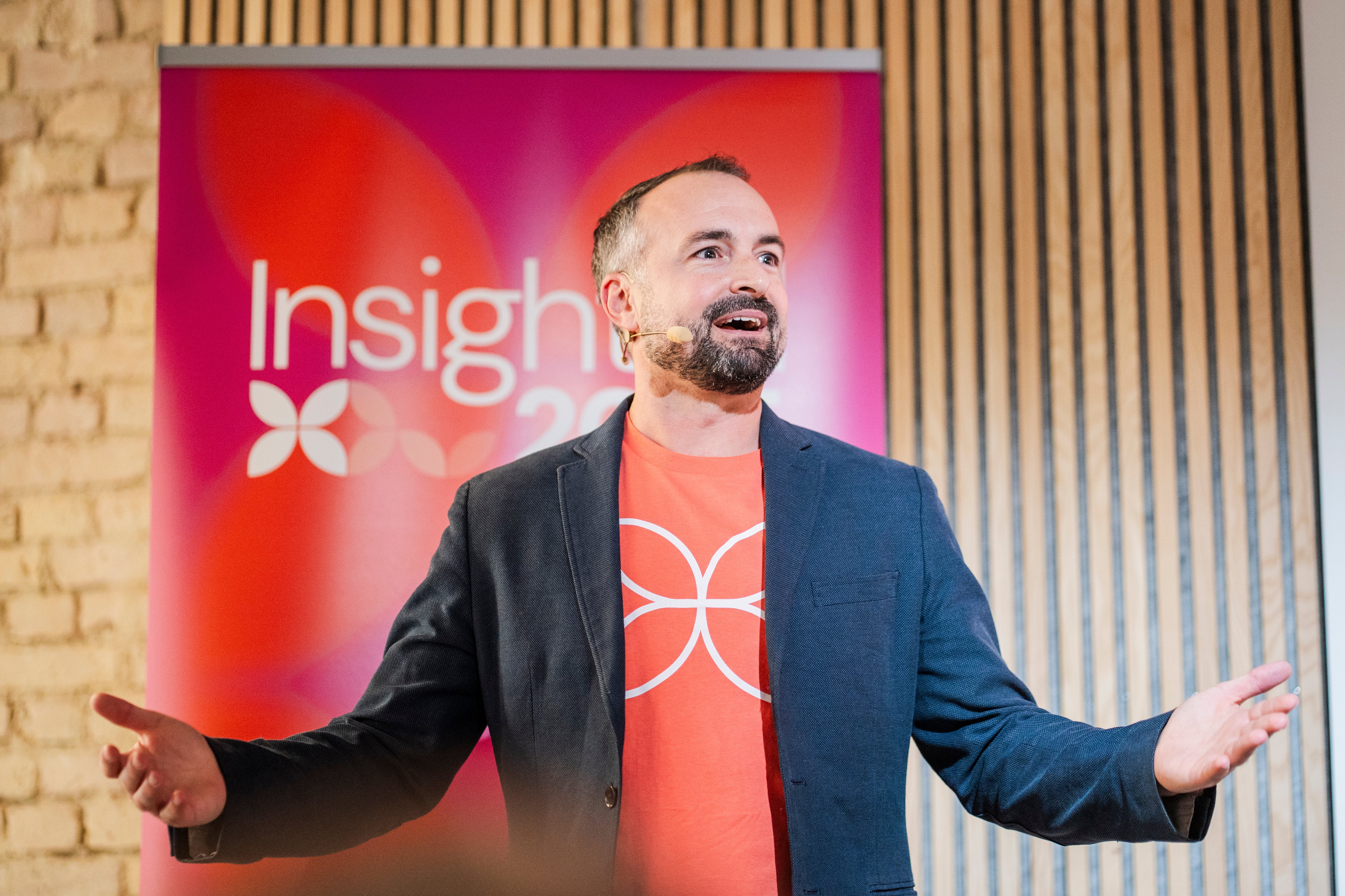 Michael Duning opening the Insightful 2025 conference. He's wearing a blue blazer and the insightful t-shirt with the logo in orange.