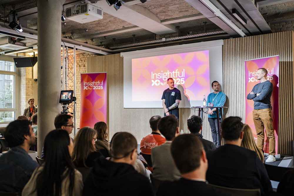On the stage of Insightful 2025 in order from the right: Antti wearing blue pullover and brown pants, Jean-Luc wearing a light blue pullover and jeans, and Teppo wearing a black t-shirt. 